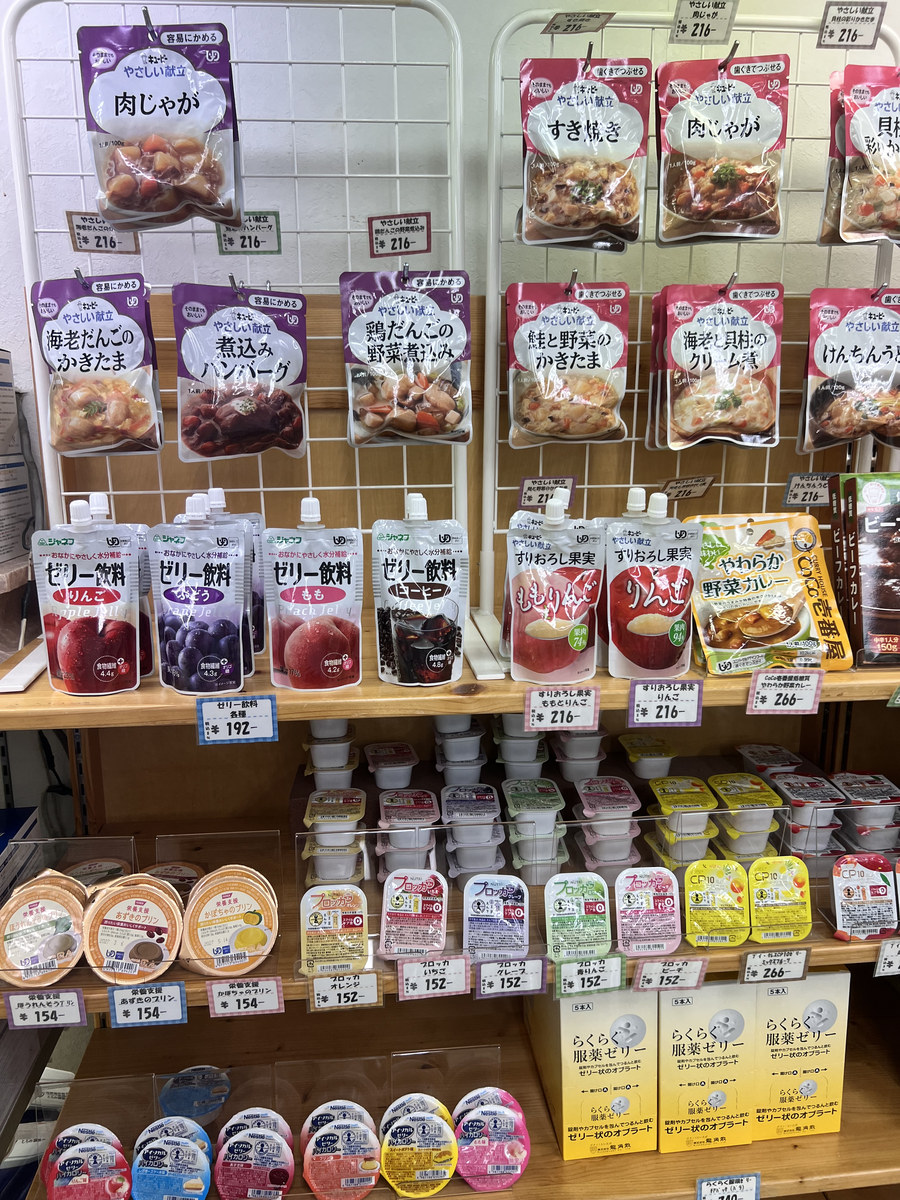 介護食売り場の棚。キユーピーやさしい献立のパウチが、区分ごとに紫と赤で色分けされて並んでいる
