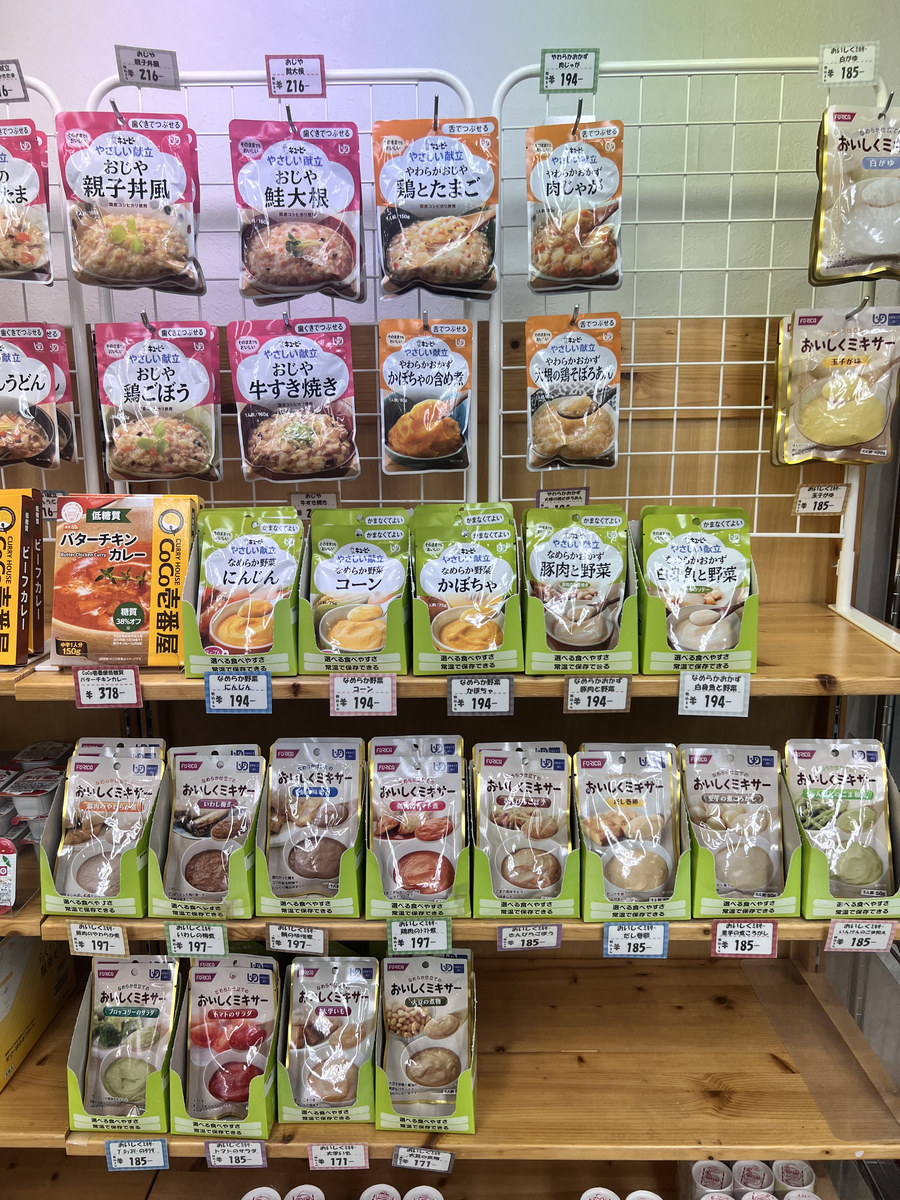 介護食売り場の棚。おじや、なめらか野菜、おいしくミキサーのパウチが並び、UDFマークのない一般のレトルトカレーも同じ棚に置かれている